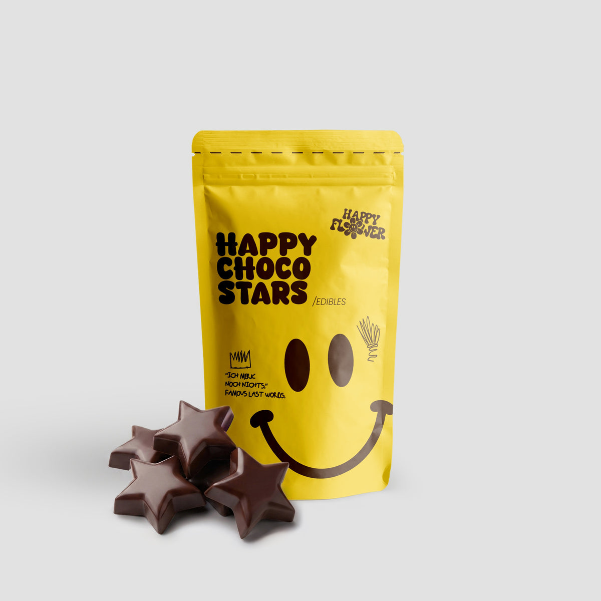 Happy Flower Happy Choco Stars Edibles in gelber Standbeutel-Verpackung mit mehreren sternförmigen Schokoladenstücken im Vordergrund auf hellem Hintergrund.
