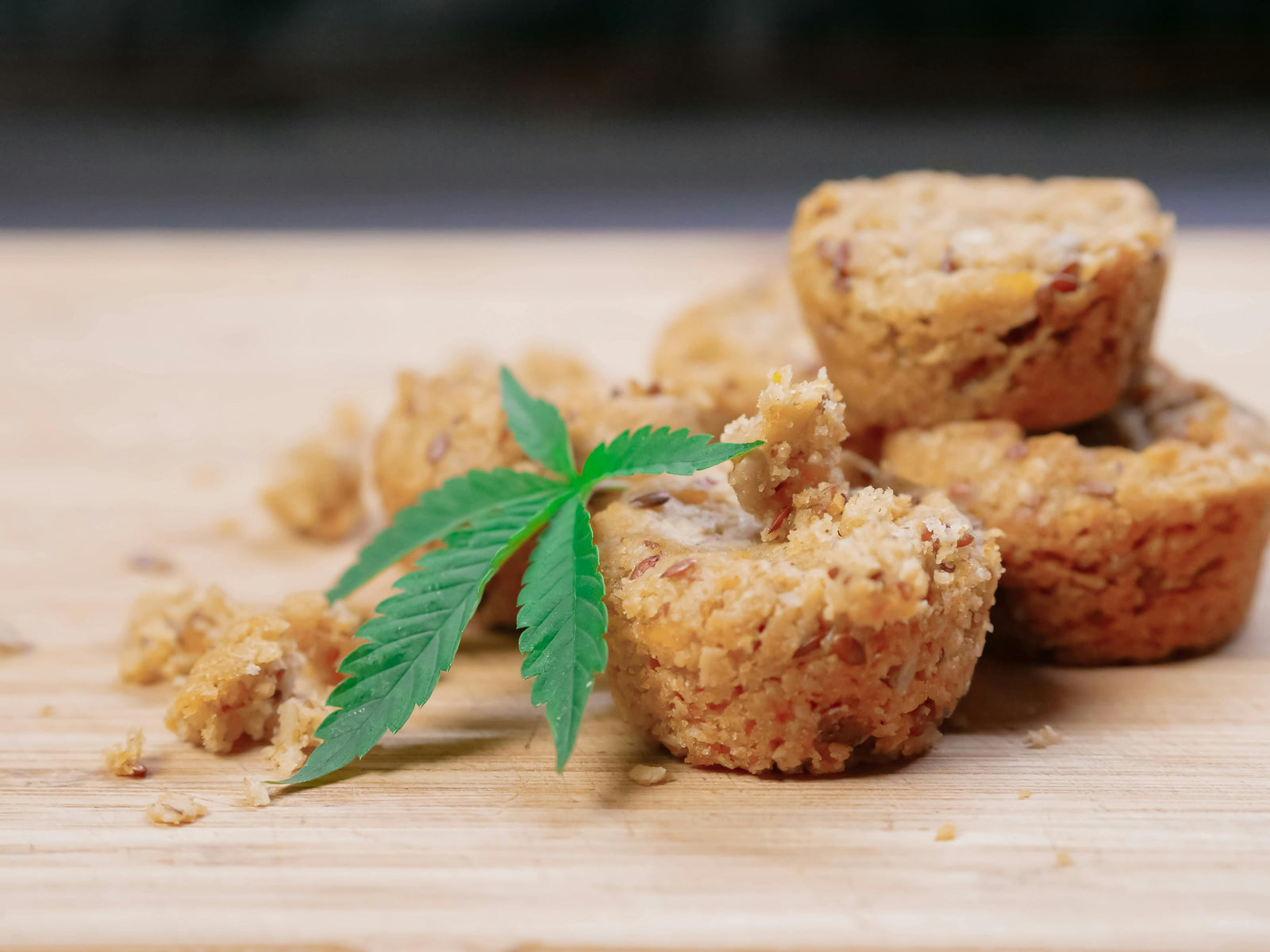 Selbstgemachte Cannabis-Brownies und Kekse auf einem Holzbrett, umgeben von frischen Hanfblättern.