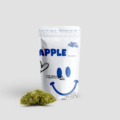 Happy Flower Apple CBD Flowers in weißer Standbeutel-Verpackung mit zwei grünen Cannabisblüten im Vordergrund auf hellem Hintergrund.