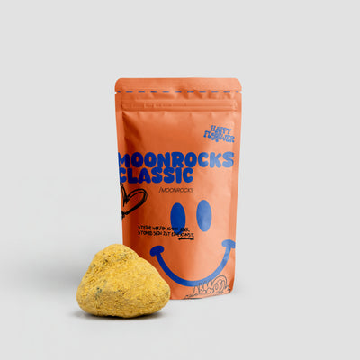 Happy Flower Moonrocks Classic in korallfarbener Standbeutel-Verpackung mit einem großen goldgelben Moonrock im Vordergrund auf hellem Hintergrund.

