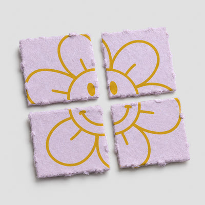 Vier quadratische, perforierte Blotter-Papiere in Helllila mit gelber, lächelnder Blumenillustration auf weißem Hintergrund.
