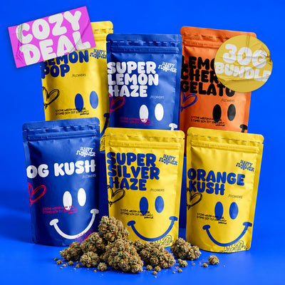 Sechs bunte Happy Flower Blüten-Baggys in Blau, Gelb und Orange, ästhetisch arrangiert vor einem kräftig blauen Hintergrund. Im Vordergrund liegt ein kleiner Haufen Blüten mit natürlichen Schatten.