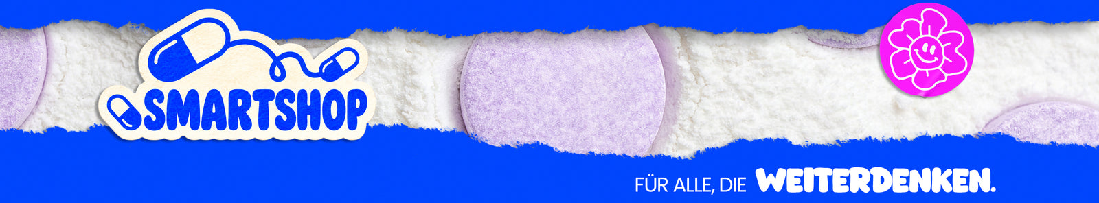 Blaues Banner mit weißen Pulverkristallen und lilafarbenen Tabletten. Links steht „Smartshop“, rechts ist ein pinkes Blumenlogo und unten der Schriftzug „Für alle, die weiterdenken.“