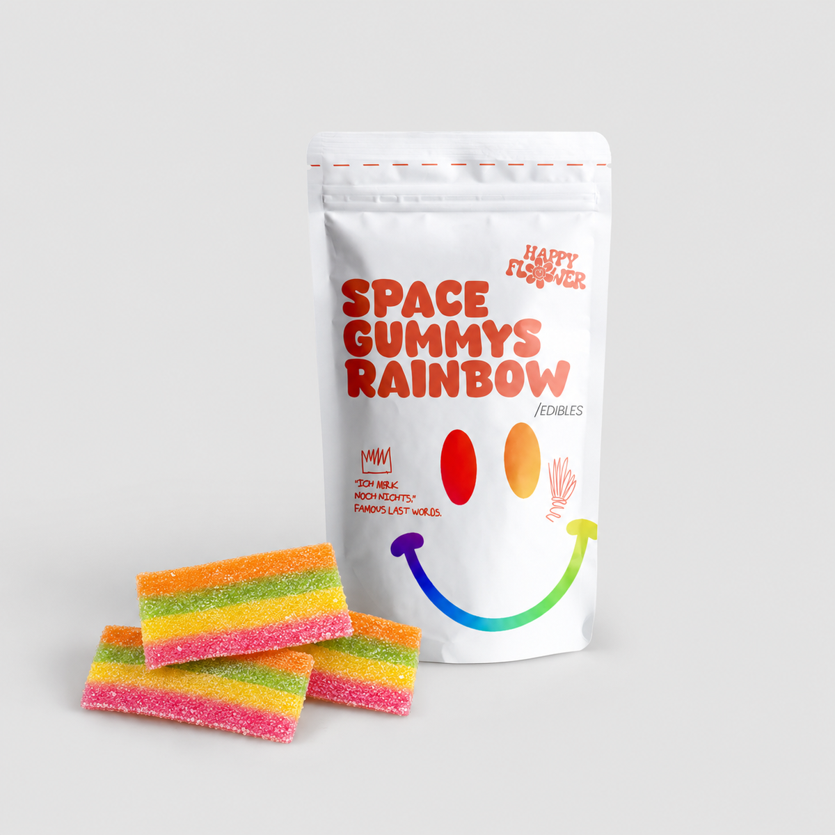 Happy Flower Space Gummys Rainbow Edibles in weißer Standbeutel-Verpackung mit mehreren bunten, gezuckerten Regenbogen-Gummistreifen im Vordergrund auf hellem Hintergrund.